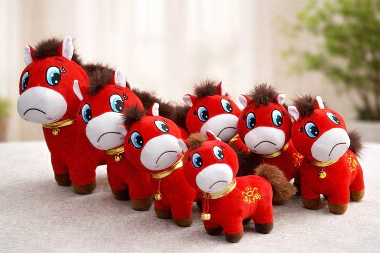 A lineup of red horse plush toys with a Chinese New Year theme, except their mouths are sewn upside down. They're displayed behind a bright backdrop with the living room behind them.
